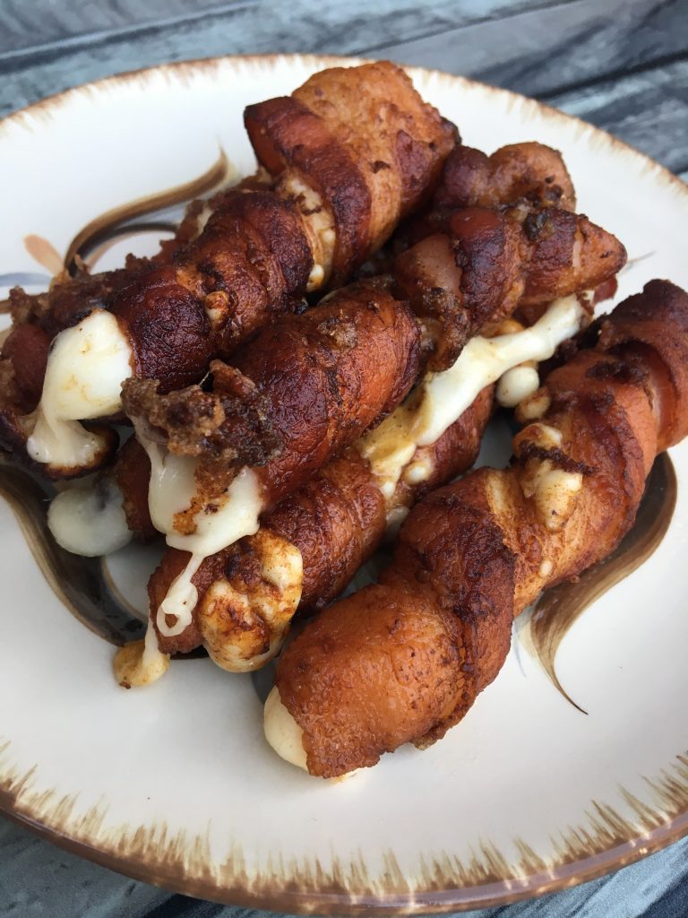 bacon wrapped cheese sticks stacked on a white plate