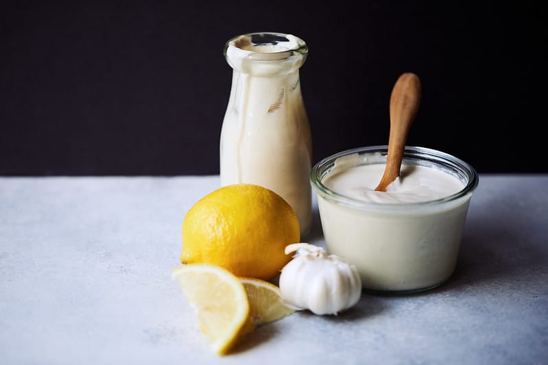 lemon tahini dressing in a jar and glass jug with lemon and garlic clove