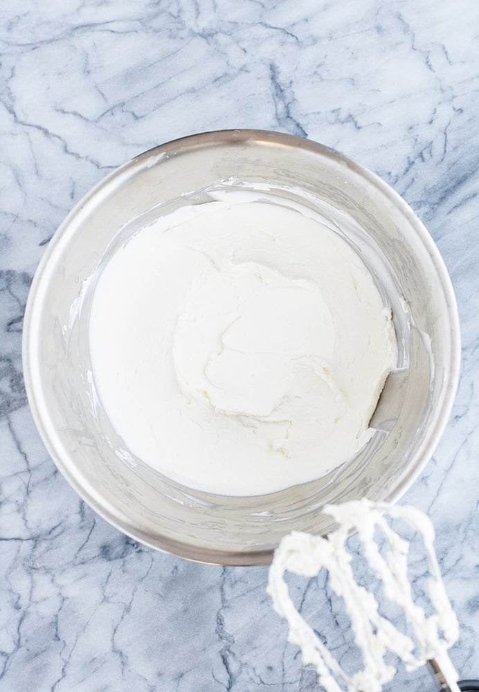cream cheese whisked with an electric mixer in a stainless steel mixing bowl