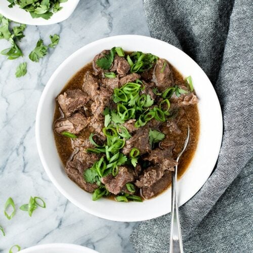 2 bowls of Keto Korean Barbecue Beef atop a marble kitchen counter beside a cloth table napkin with a small bowl of chopped fresh cilantro on the side