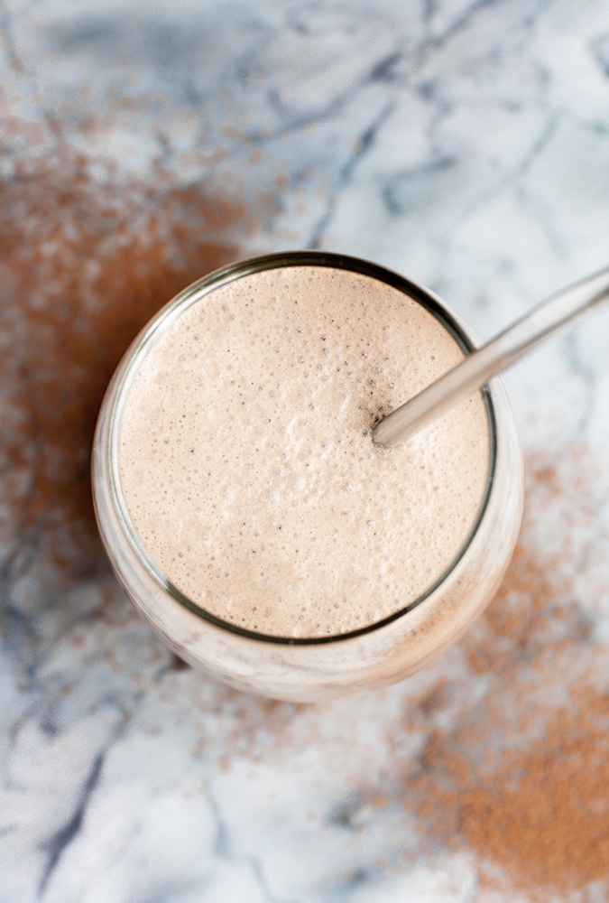 overhead shot of chocolate fat bomb smoothie in a glass with a stainless steel straw atop a marble kitchen counter