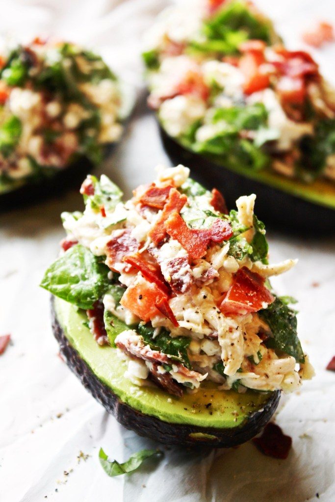 3 blt chicken salad stuffed avocados on a wooden surface