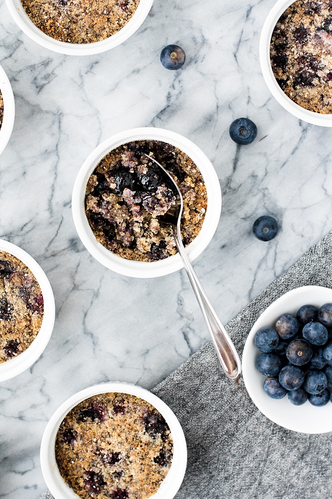 keto Blueberry Crumble with a spoon beside three blueberries and a small plate of fresh blueberries