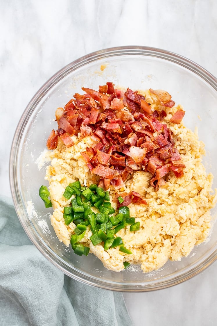 Low-Carb Cheddar Scone dough with chopped cooked bacon bits and chopped jalapeño in a mixing bowl