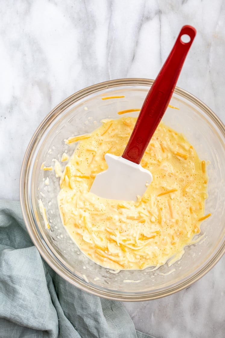 a medium bowl with egg batter, mozzarella and cheddar mixed together using a rubber spatula