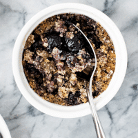 hero shot of Blueberry Breakfast Crumble in a ramekin with a spoon atop a marble kitchen counter