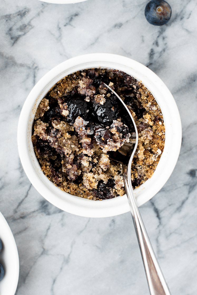 hero shot of Blueberry Breakfast Crumble in a ramekin with a spoon atop a marble kitchen counter