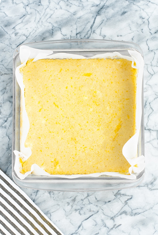baked keto lemon bars whole in a baking dish lined with parchment paper atop a marble kitchen counter