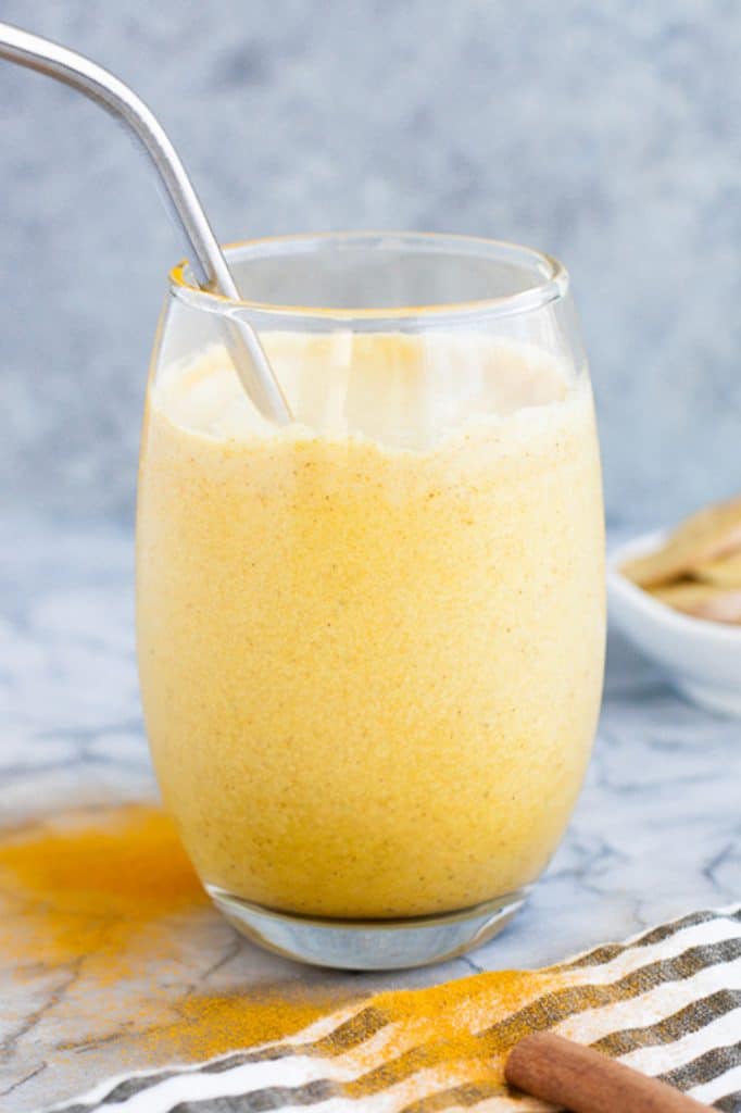 a glass of Keto Golden Smoothie with a stainless steel straw atop a marble kitchen counter