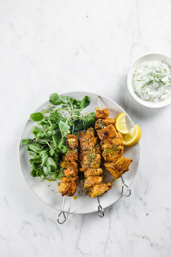 3 skewers of Keto Chicken Shawarma Kebabs served on a platebeside tzatziki dip atop a marble kitchen counter