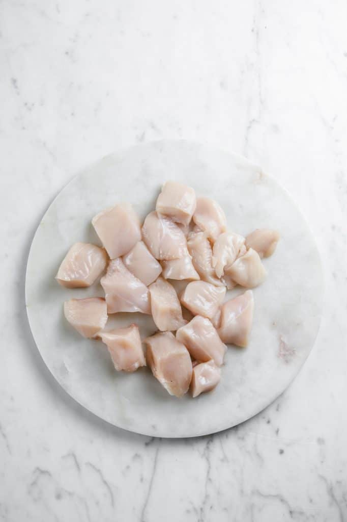 raw chicken breast chopped into cubes atop a marble plate