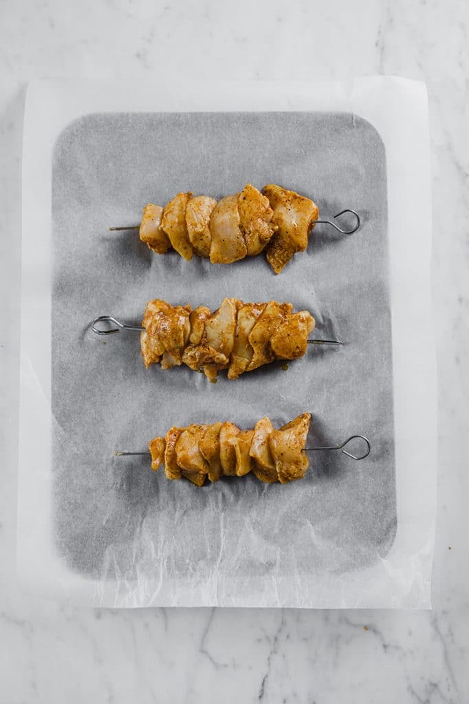 3 skewers of chicken kebabs placed on a baking tray lined with parchment paper
