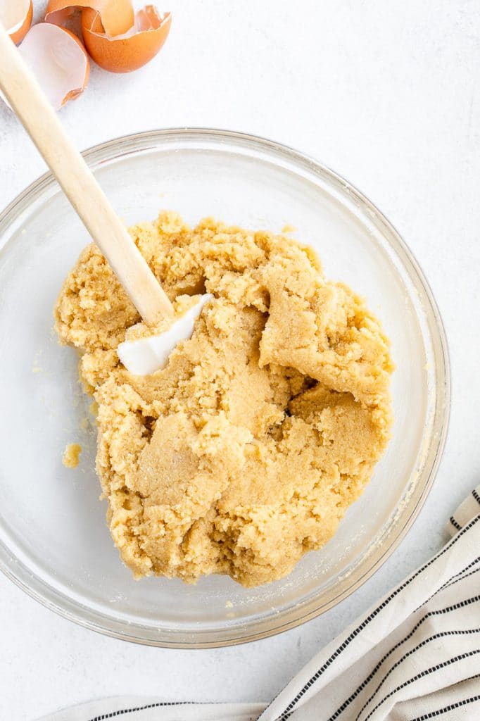 keto cookie dough mixed with a rubber spatula in a glass mixing bowl atop a marble kitchen counter