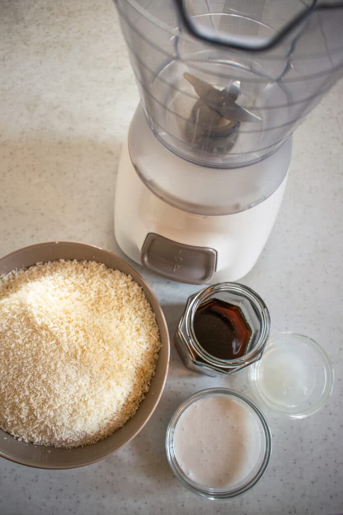 blender, maple syrup, coconut cream, coconut oil, shredded coconut atop a kitchen counter