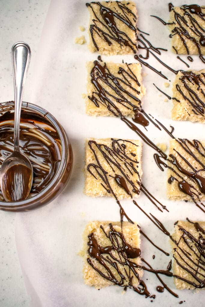 coconut bars drizzled with melted dark chocolate on a baking sheet lined with parchment paper