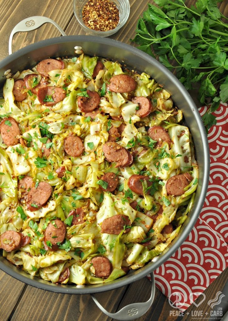 fried cabbage with kielbasa in a skillet with parsley and red pepper beside it