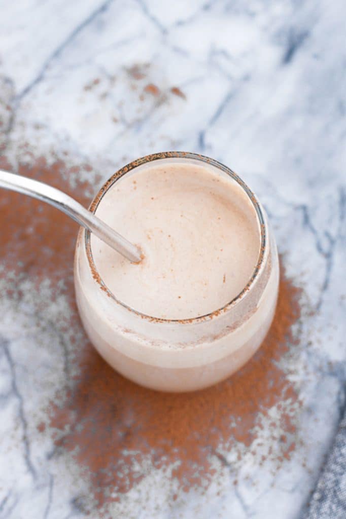 overhead shot of a glass of keto mocha smoothie with a stainless steel straw atop a marble kitchen counter