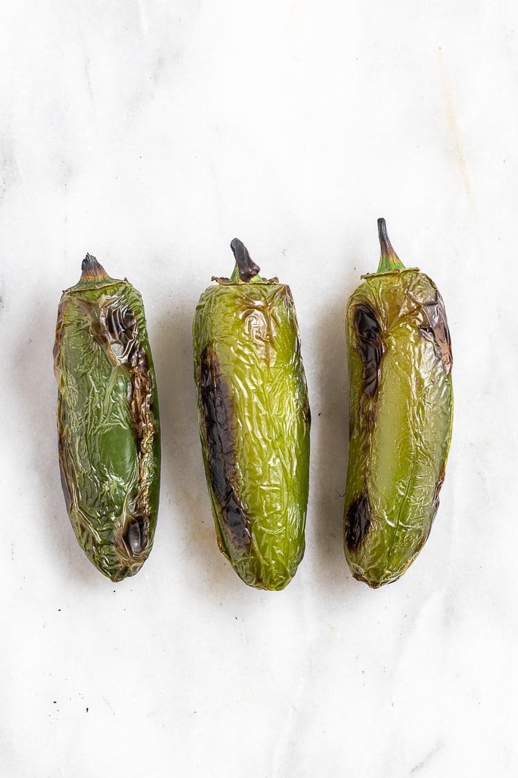 3 roasted jalapeno peppers on a marble kitchen counter