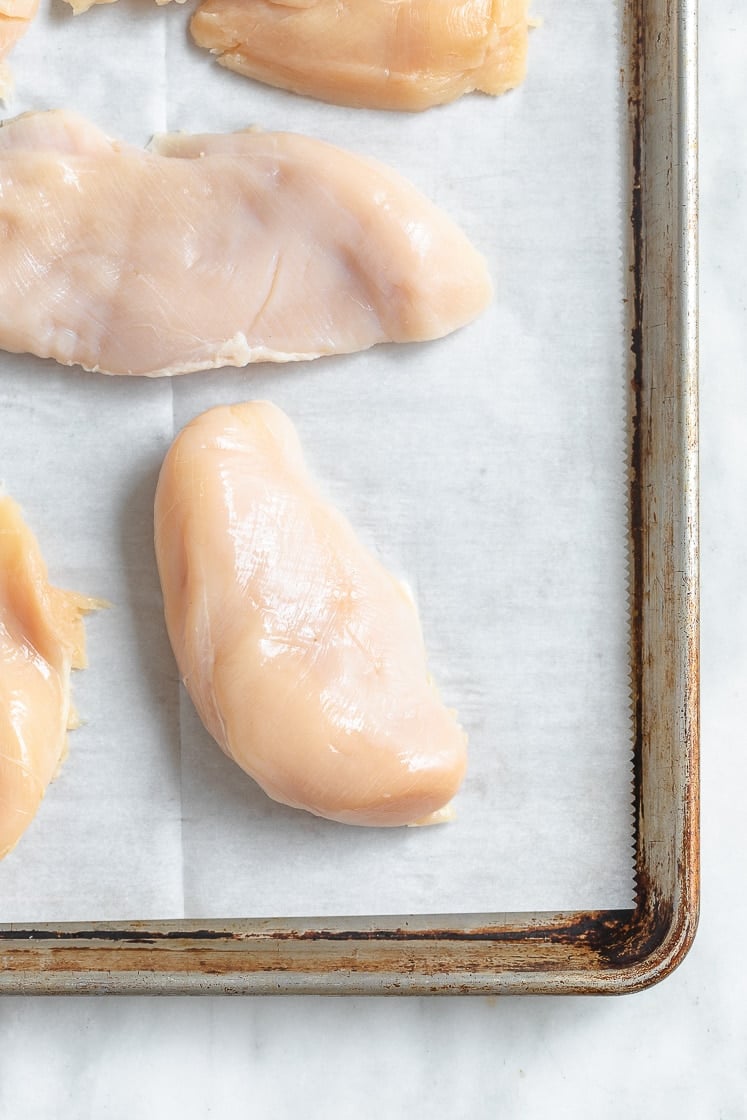 raw chicken breasts on a baking tray lined with parchment paper