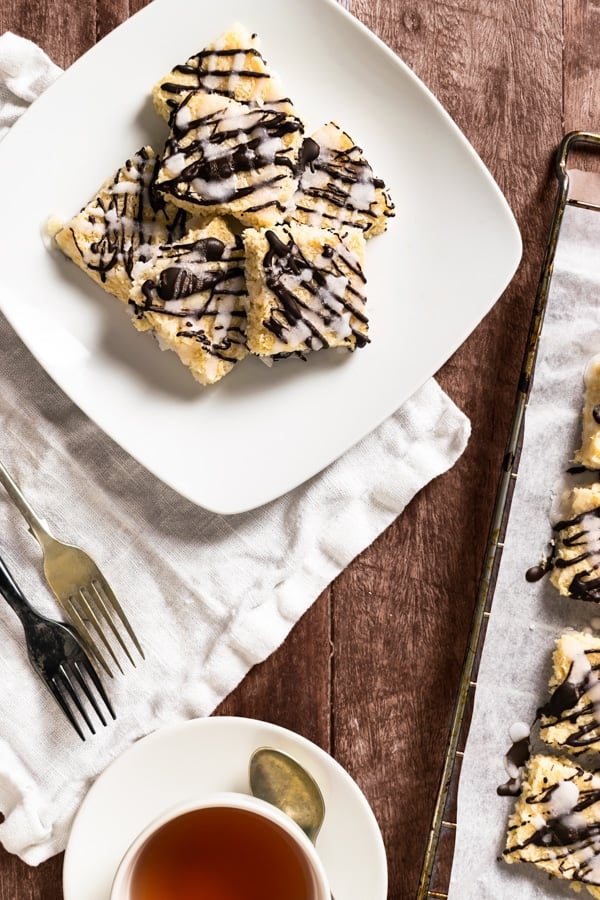 6 Low Carb Chocolate & Vanilla Glazed Coconut Bars on a plate beside a cup of tea, forks and a table napkin
