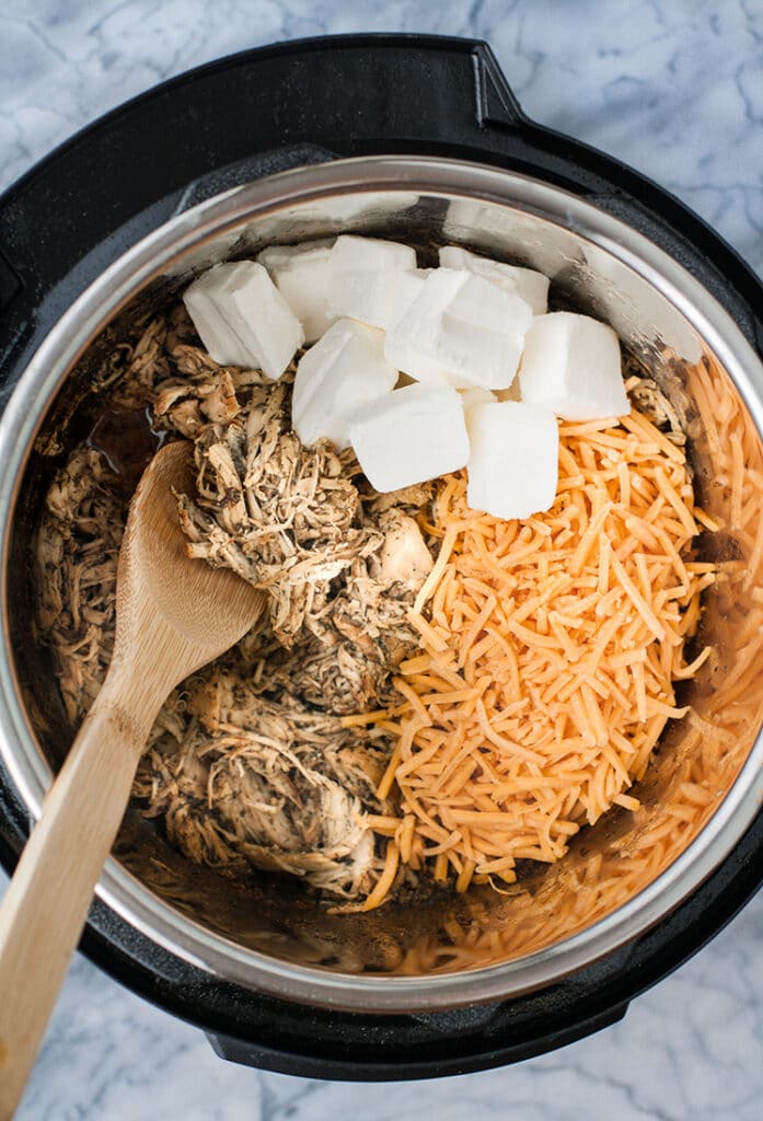 Keto Creamy Ranch Chicken Freezer meal in an instant pot with cubed cream cheese and shredded cheddar