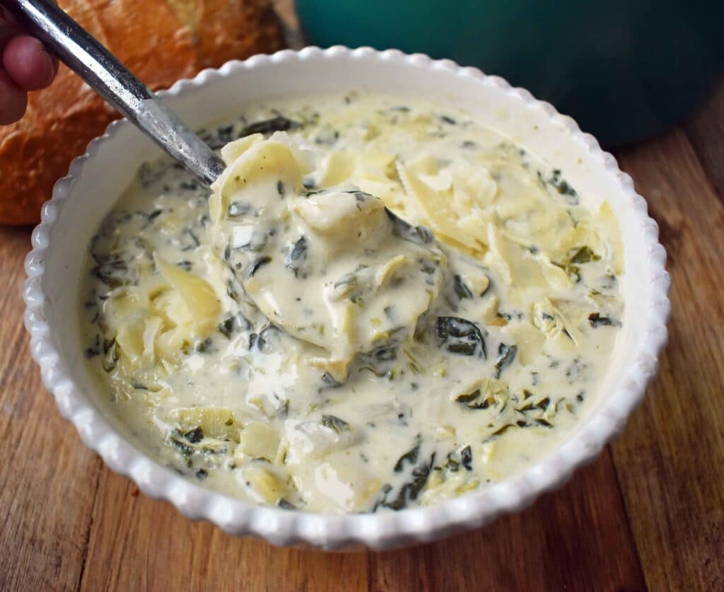 a bowl of Creamy Spinach Artichoke Soup being scooped with a spoon