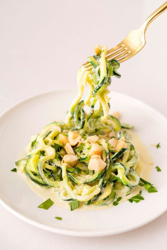 vegan keto alfredo zoodles on a white plate eaten with a golden fork