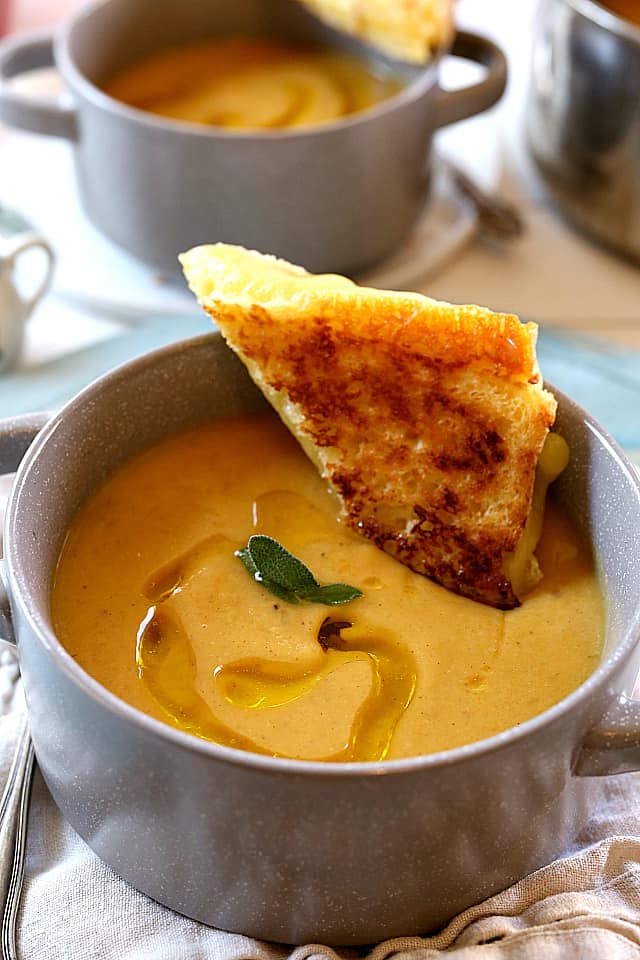 a bowl of Roasted Butternut Squash Apple Soup with a bread stick being dipped