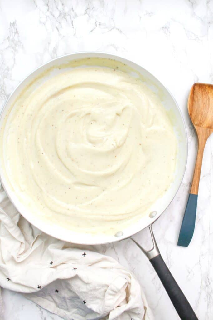 creamy vegan cauliflower sauce in a pan beside a wooden spoon