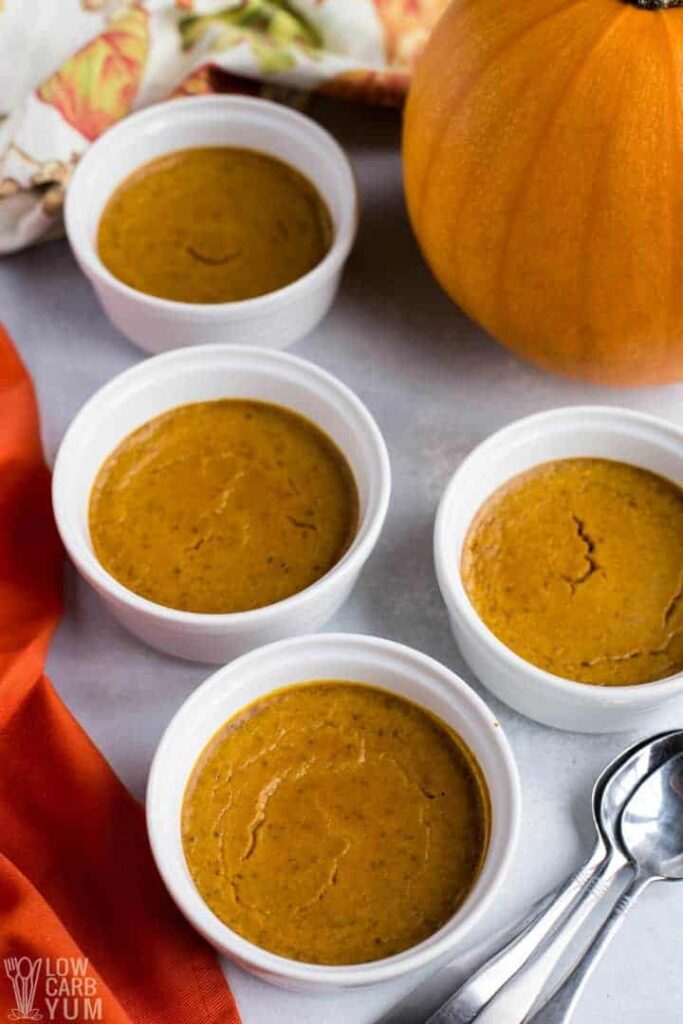 healthy paleo pumpkin custard in small bowls beside teaspoons and a pumpkin