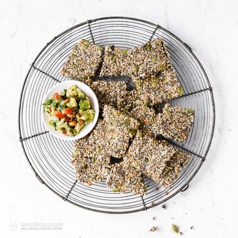 Crispy Multiseed Keto Crackers on a cooling rack with a small plate of guacamole