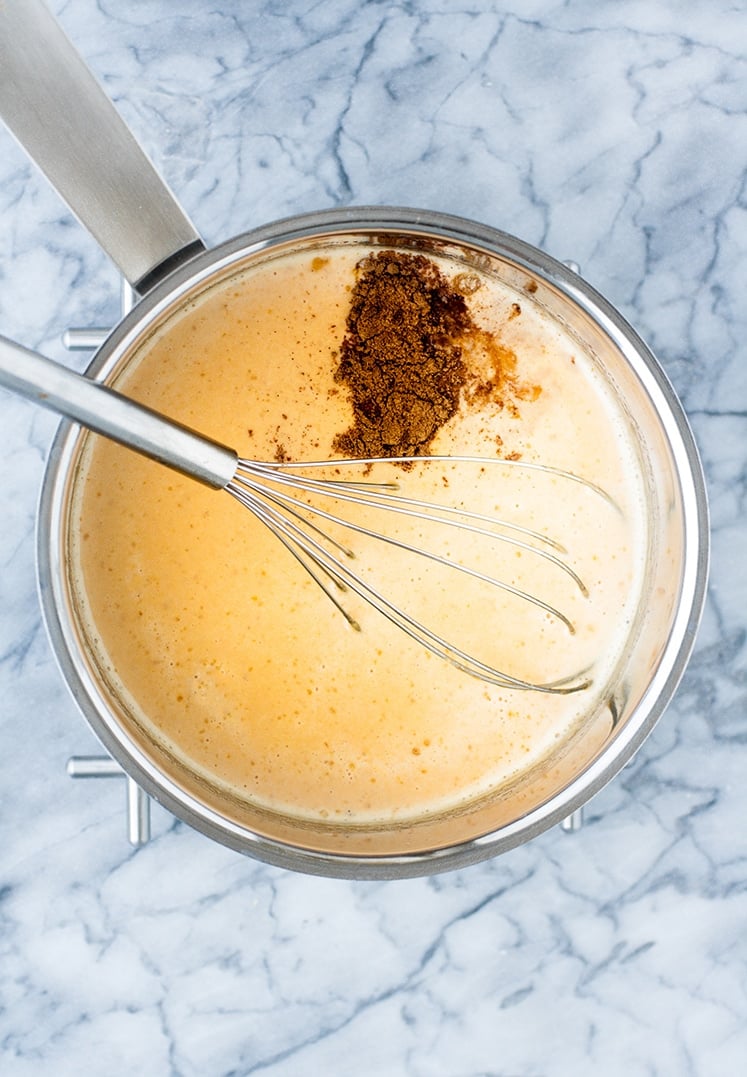 overhead shot of heavy cream mixture, pumpkin pie spice, vanilla extract and whisk in a saucepan