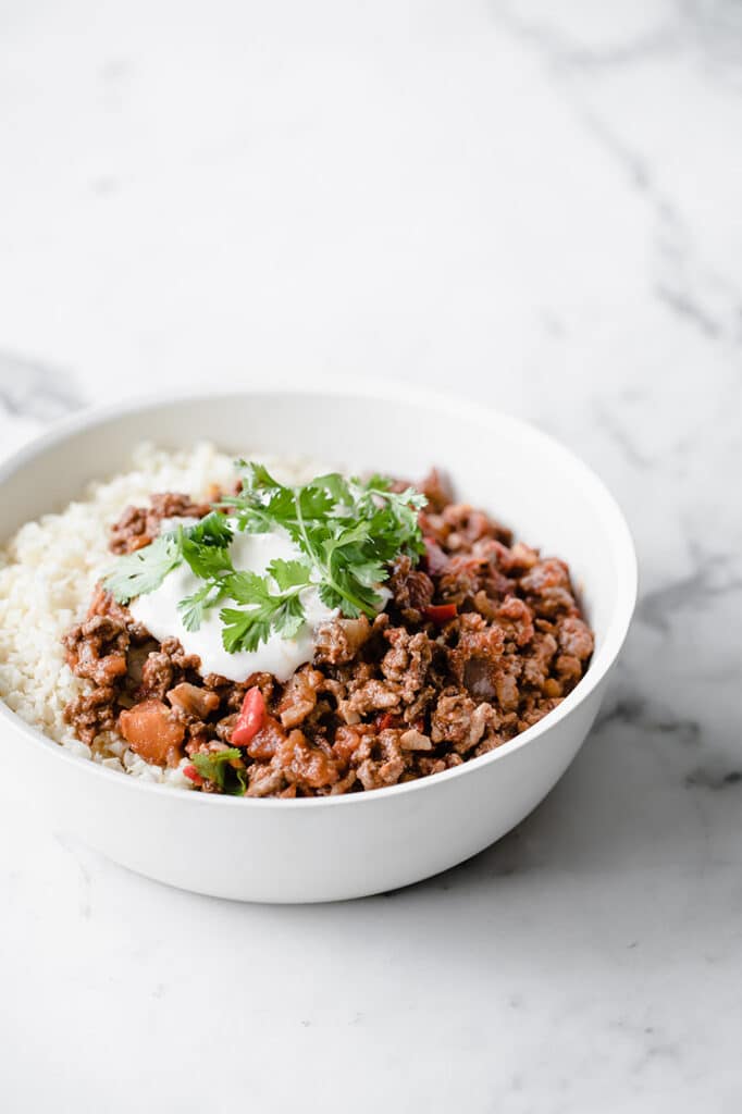 a bowl of keto chili con carne and cauliflower rice atop a marble kitchen counter
