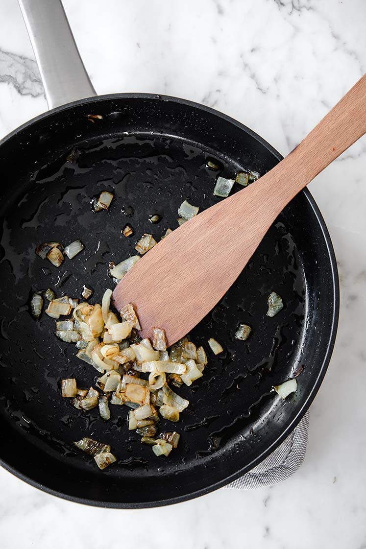 chopped onions being sautéed in olive oil on a large pan