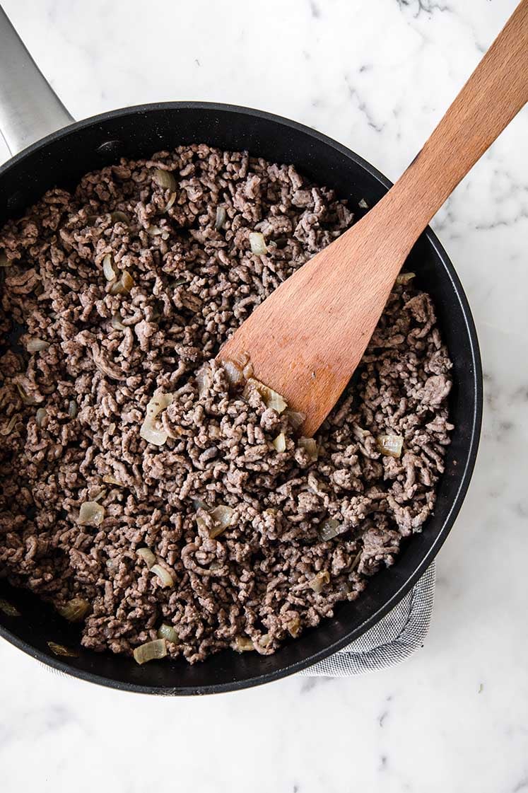 sautéed ground beef beeing stirred with a wooden spoon on a large pan