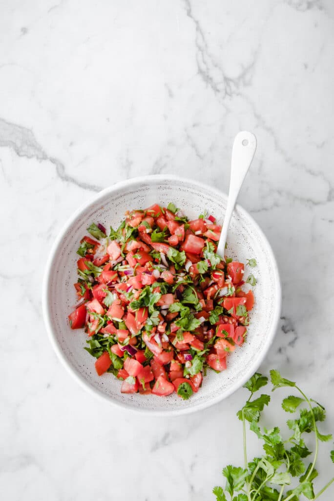overhead shot of a bowl of easy keto salsa with a spoon atop a marble kitchen counter