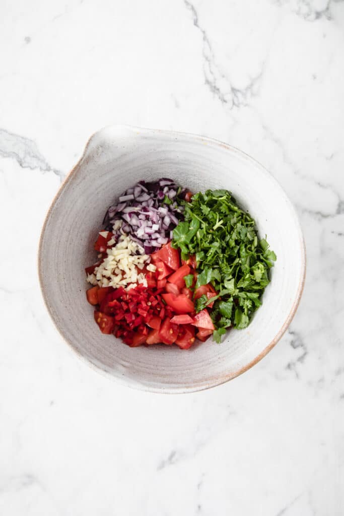 a mixing bowl with easy keto salsa ingredients atop a marble kitchen counter