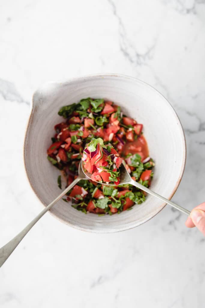Easy keto salsa being mixed in a mixing bowl atop a marble kitchen counter