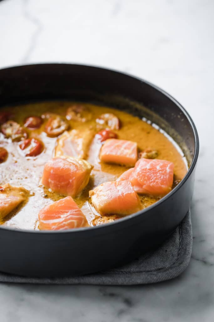 cubed salmon added to curry on a pan