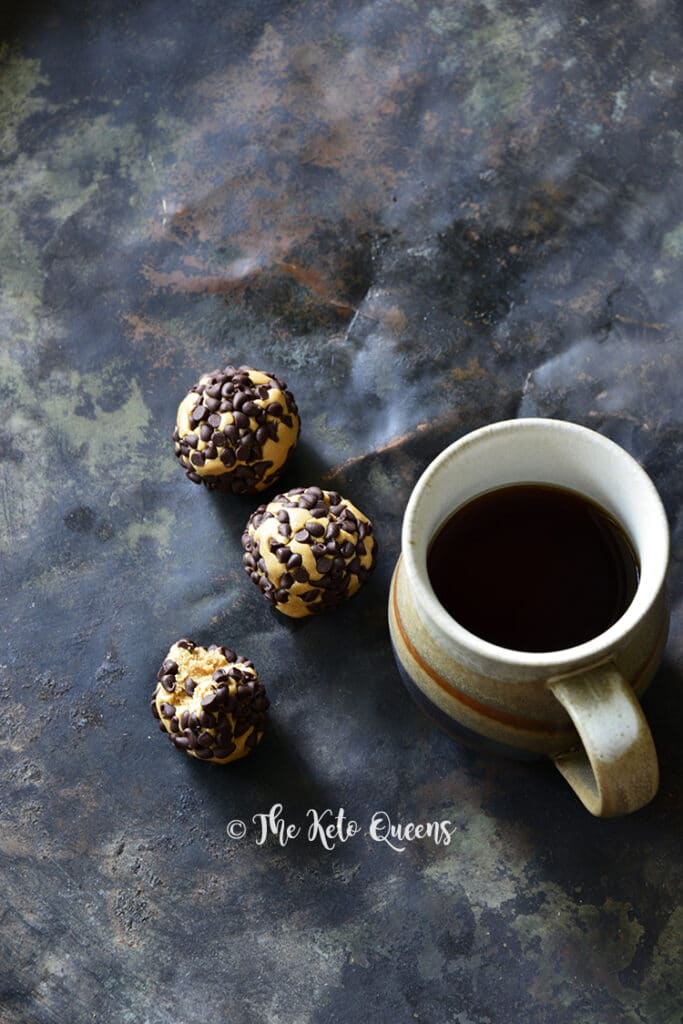 3 keto chocolate peanut butter protein bites with a cup of coffee on the side atop a marble kitchen counter