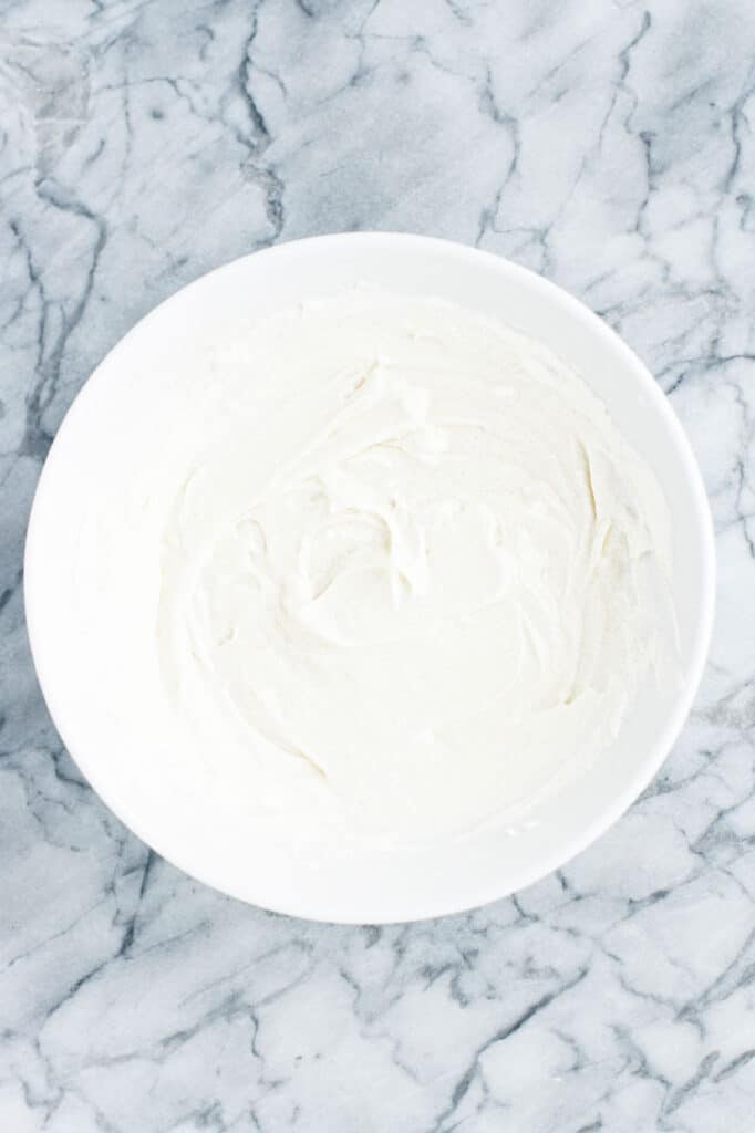 keto cinnamon roll muffin frosting in a mixing bowl atop a marble kitchen counter