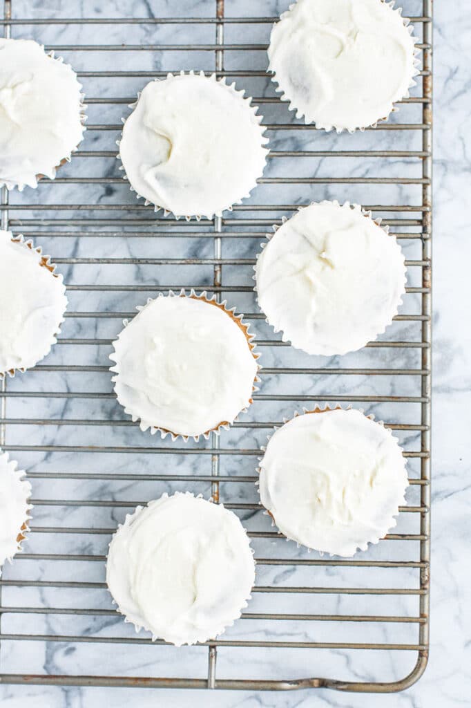 muffins with frosting on a cooling rack atop a marble kitchen counter