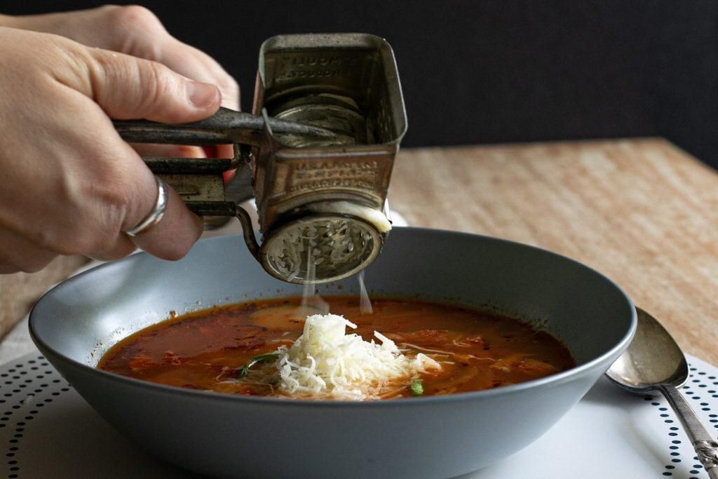 mozzarella cheese being topped on a bowl of pizza soup with zucchini atop a wooden table