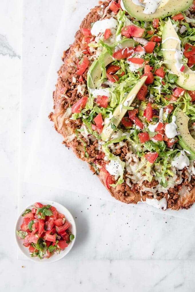 overhead shot of Keto Fathead Taco Pizza with keto salsa at the side atop a marble kitchen counter