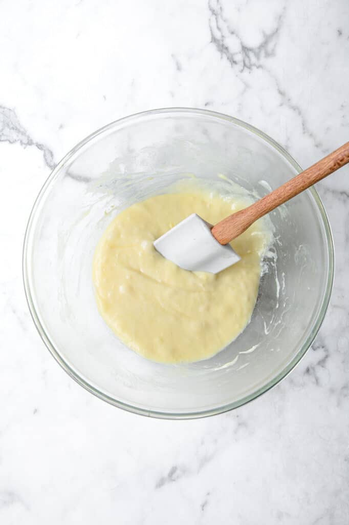 melted mixture of cheese and eggs being stirred with spatula in a glass mixing bowl atop a marble kitchen table counter