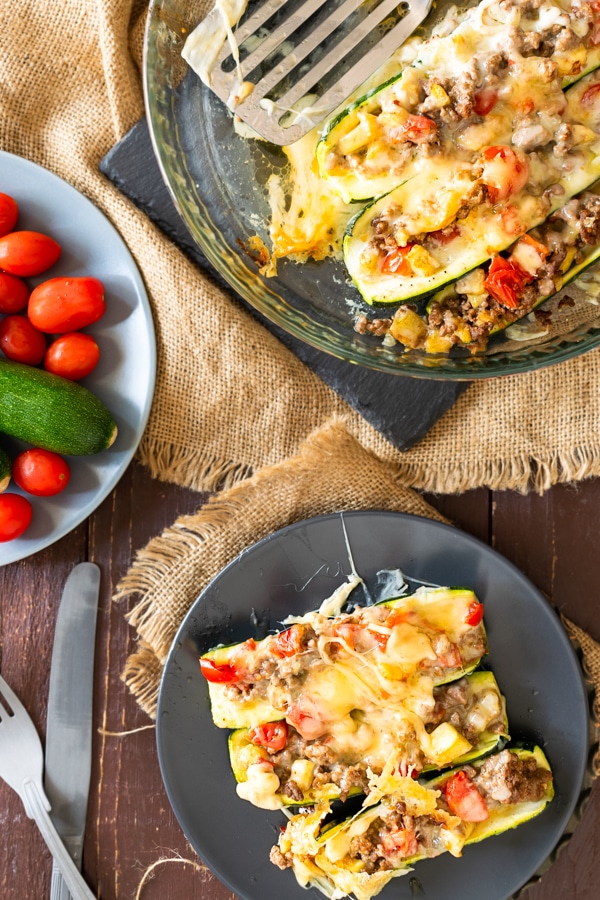 3 zucchini burrito boats on a plate with cherry tomatoes at the back ground atop a wooden table