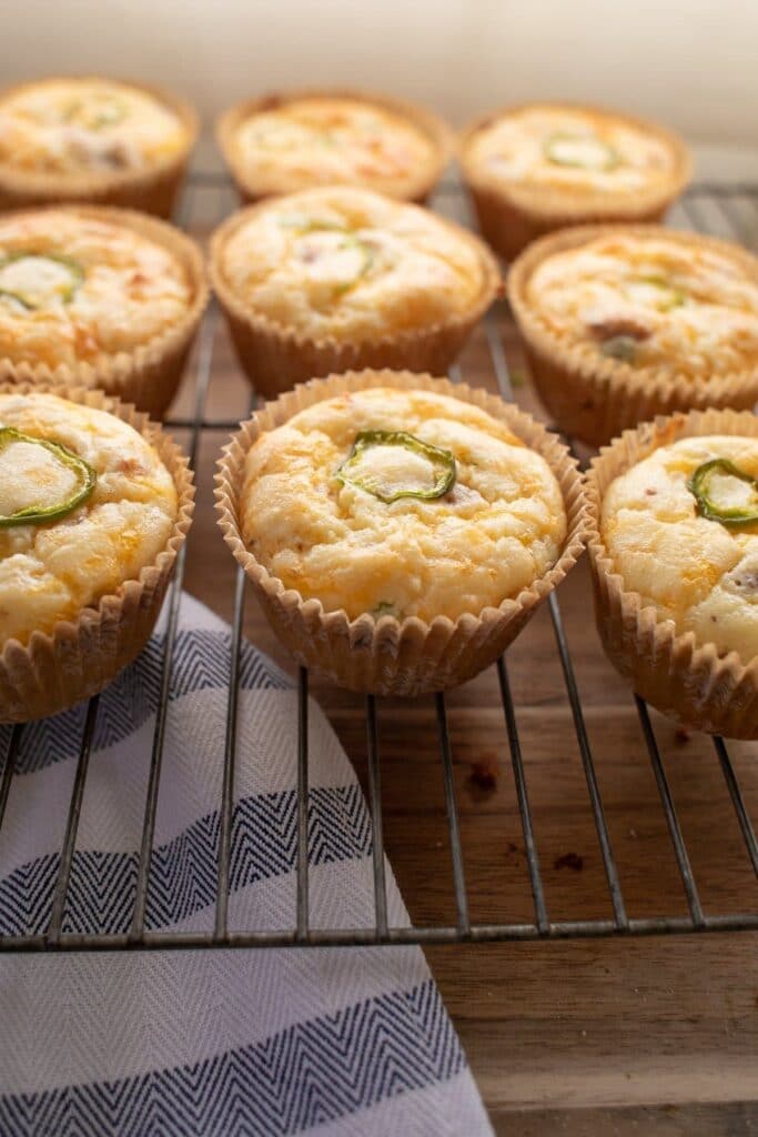 a batch of bacon jalapeño popper muffins on a cooling rack atop a wooden table