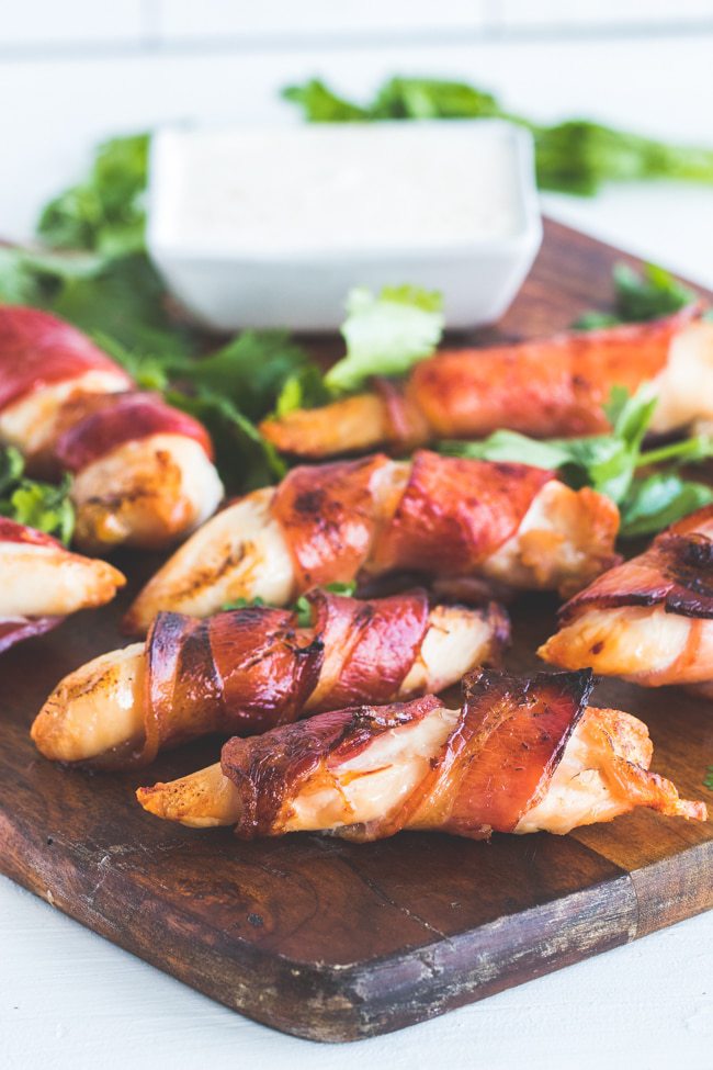 close-up shot of bacon wrapped chicken tenders on a wooden plate atop a marble kitchen table