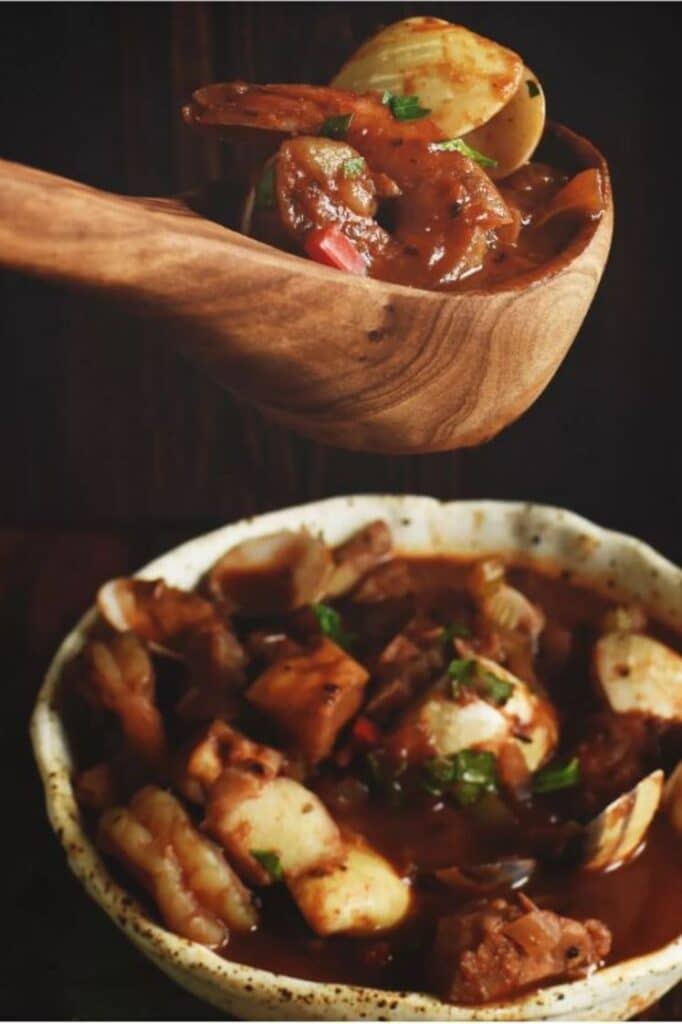 a bowl of cioppino seafood stew and a wooden ladel with a scoop of cioppino seafood stew