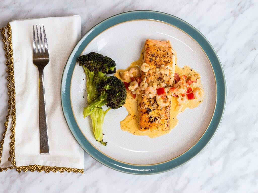 creamy cajun salmon with shrimp on a plate with broccoli on the side atop a marble kitchen counter